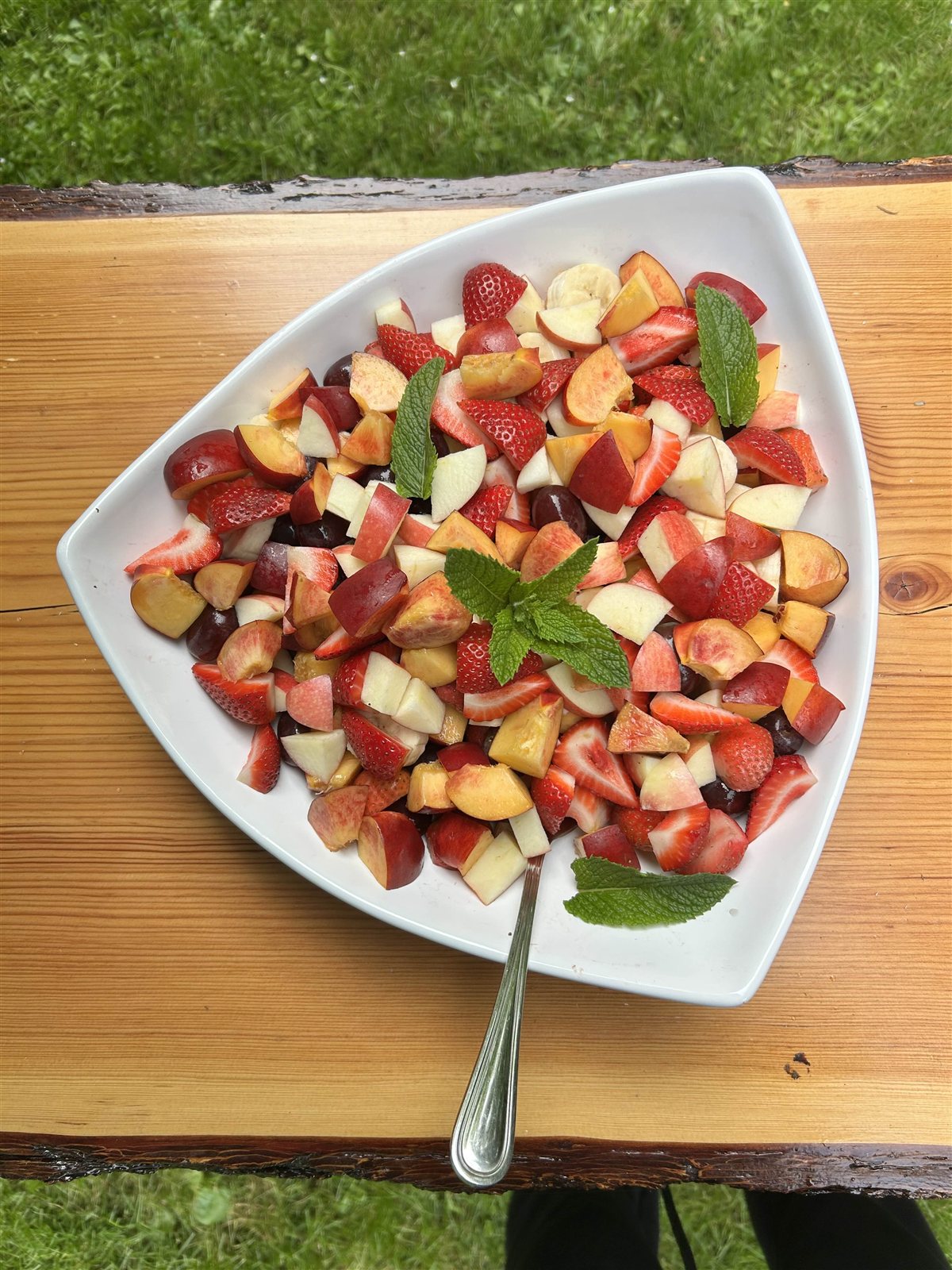 Platter of fresh fruit with strawberries, stone fruit, and mint